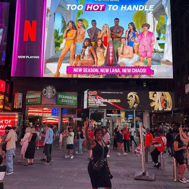 Demari Davis's mother, Vivian Davis taking pictures in front of her son's show banner in Times Square, New York City